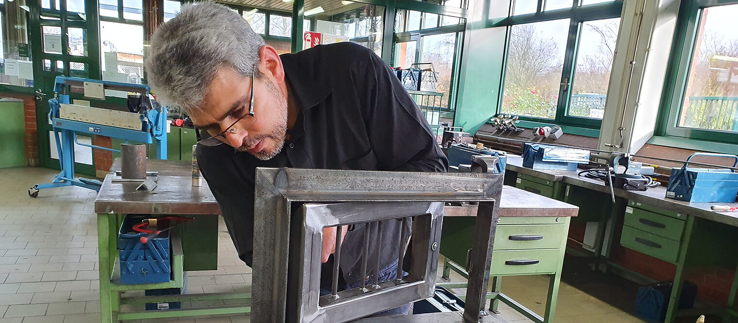 Mann arbeitet in einer Werkstatt an einem Metallrahmen.