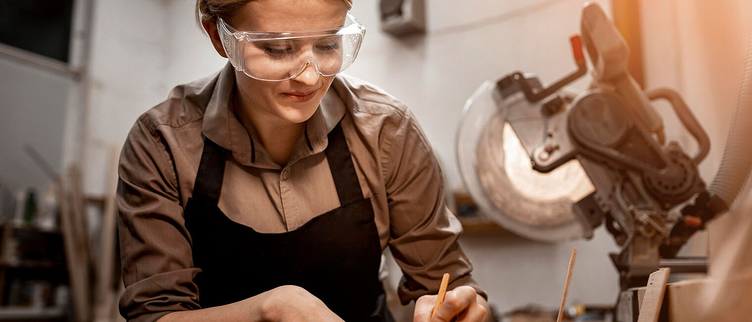 Eine Frau mit Schutzbrille arbeitet an einer Maschine.