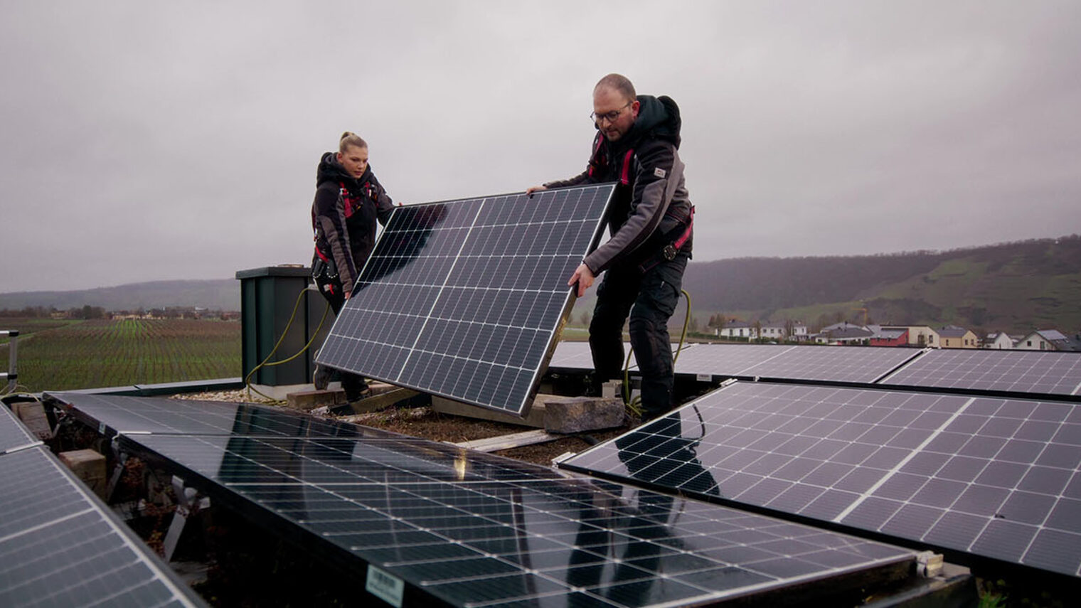 Zwei Handwerker installieren eine Photovoltaikanlage auf einem Dach.