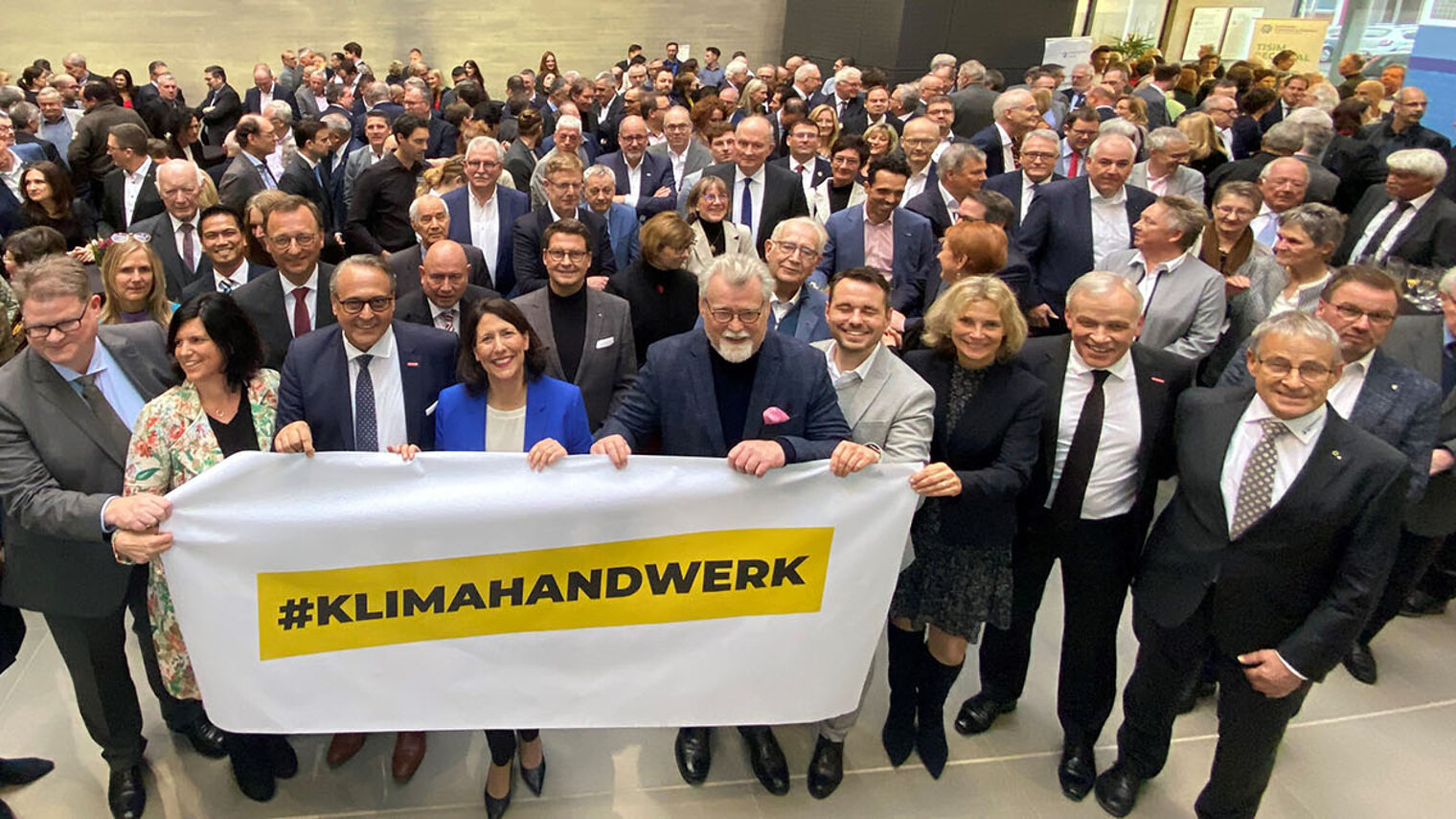 Kampagnenpartner und Gäste halten das Banner "#Klimahandwerk" hoch.