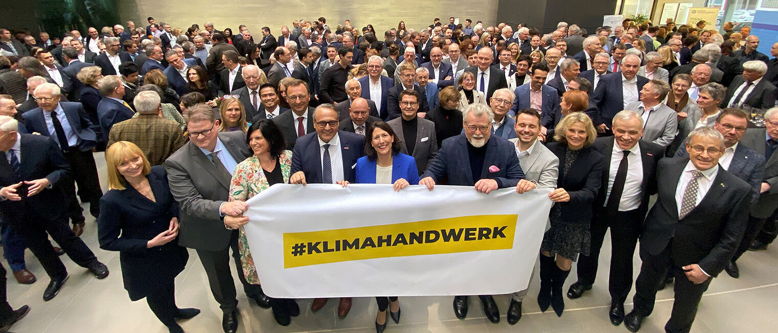 Kampagnenpartner und Gäste halten das Banner "#Klimahandwerk" hoch.