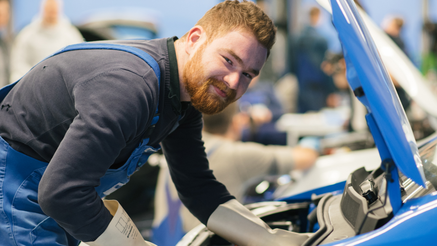 Ein Kfz-Mechatroniker arbeitet am Motorraum eines Autos.