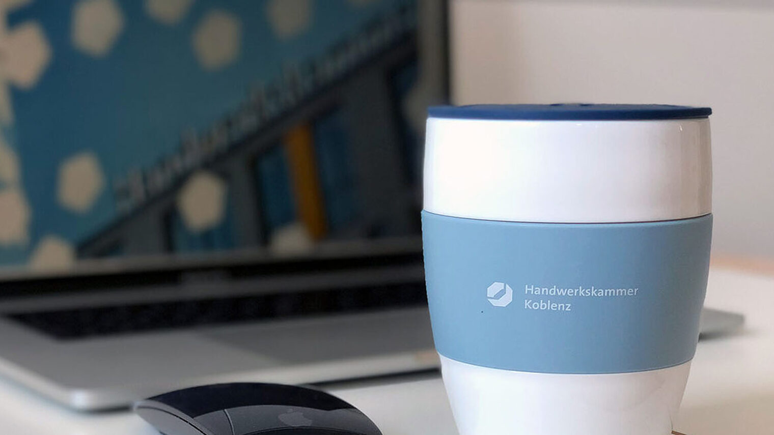Ein Kaffeebecher steht vor einem Laptop
