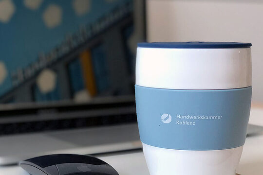 Ein Kaffeebecher steht vor einem Laptop