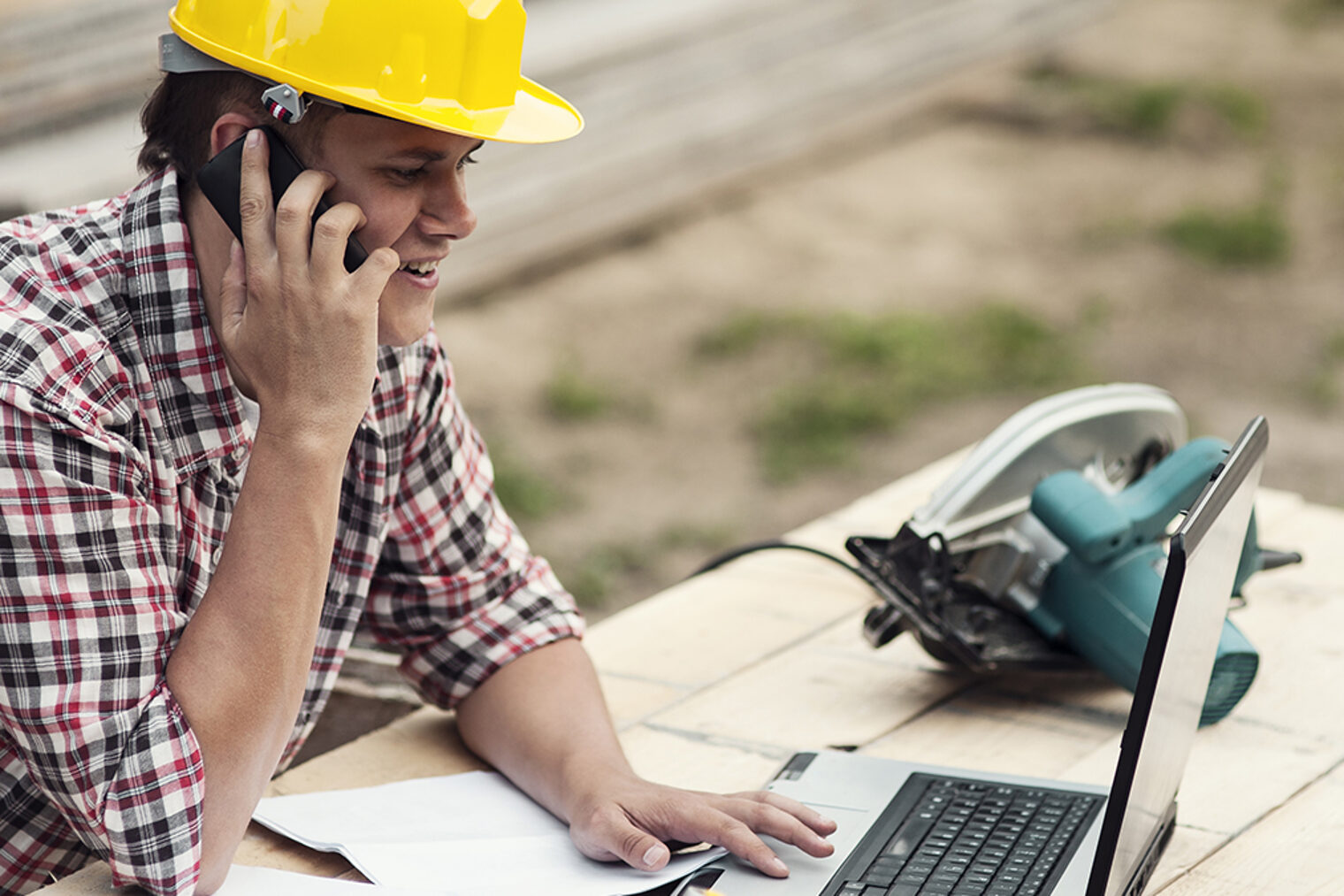 Handwerker telefoniert auf der Baustelle Handwerker auf der Baustelle telefoniert und schaut auf den aufgeklappten Laptop
