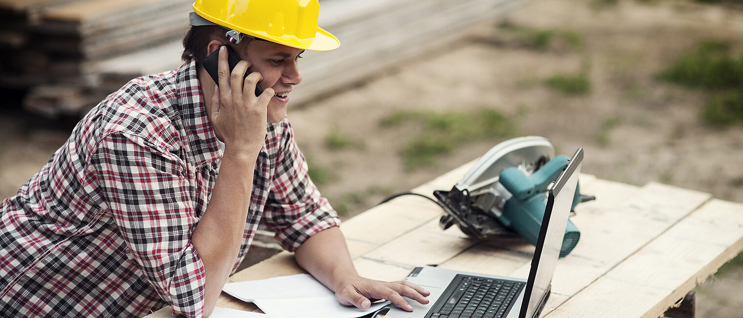 Handwerker telefoniert auf der Baustelle Handwerker auf der Baustelle telefoniert und schaut auf den aufgeklappten Laptop