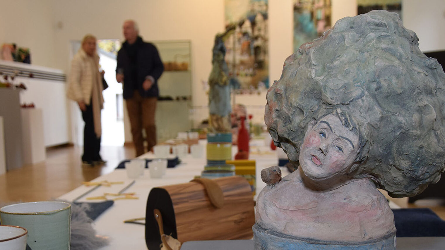 Im Vordergrund verschiedene Ausstellungsobjekte, im Hintergrund Besucher im Gespräch