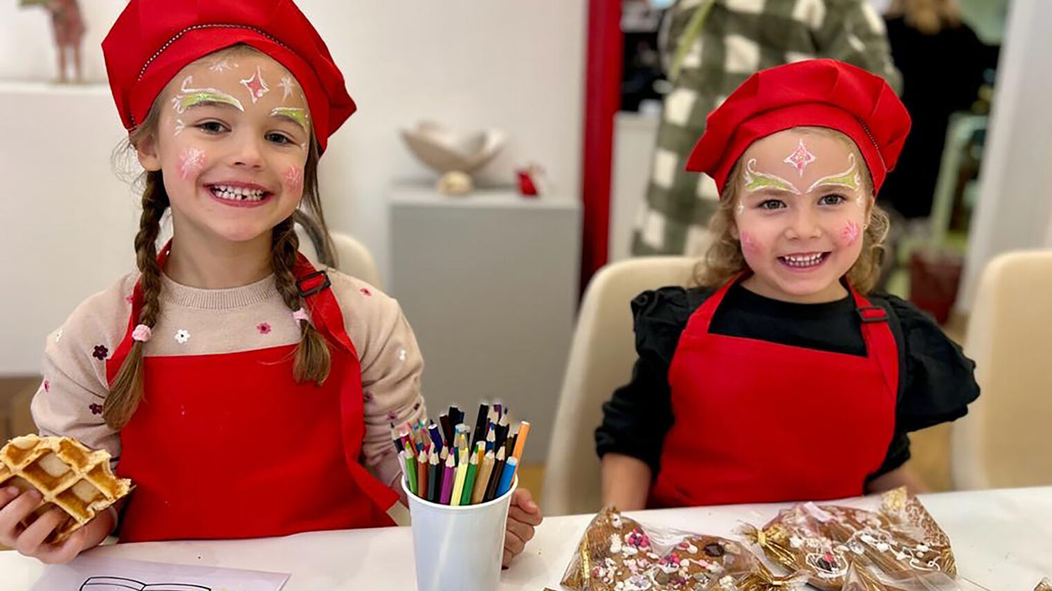 Zwei Kinder mit Backschürze und Backhaube lächeln in die Kamera. Vor ihnen liegen verzierte Lebkuchen.