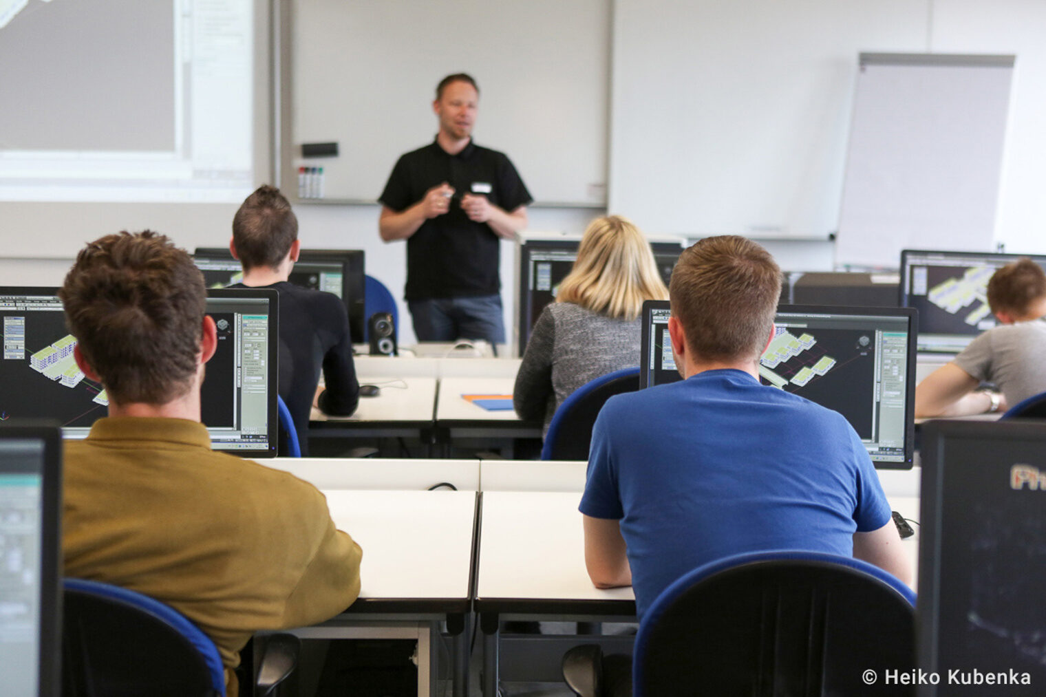 Ein Dozent erklärt etwas den Kursteilnehmern. Kursteilnehmer sitzen in einer Klasse, während der Dozent etwas erklärt.