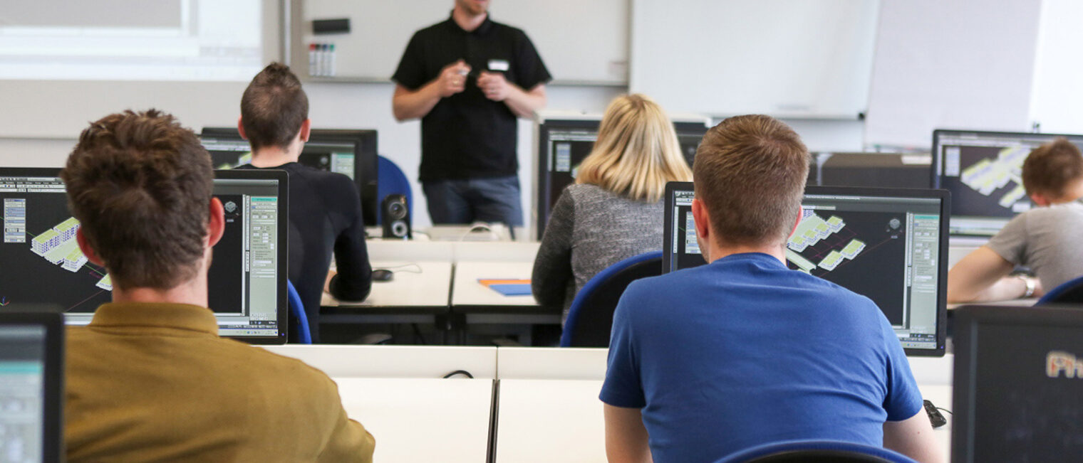 Ein Dozent erklärt etwas den Kursteilnehmern. Kursteilnehmer sitzen in einer Klasse, während der Dozent etwas erklärt.