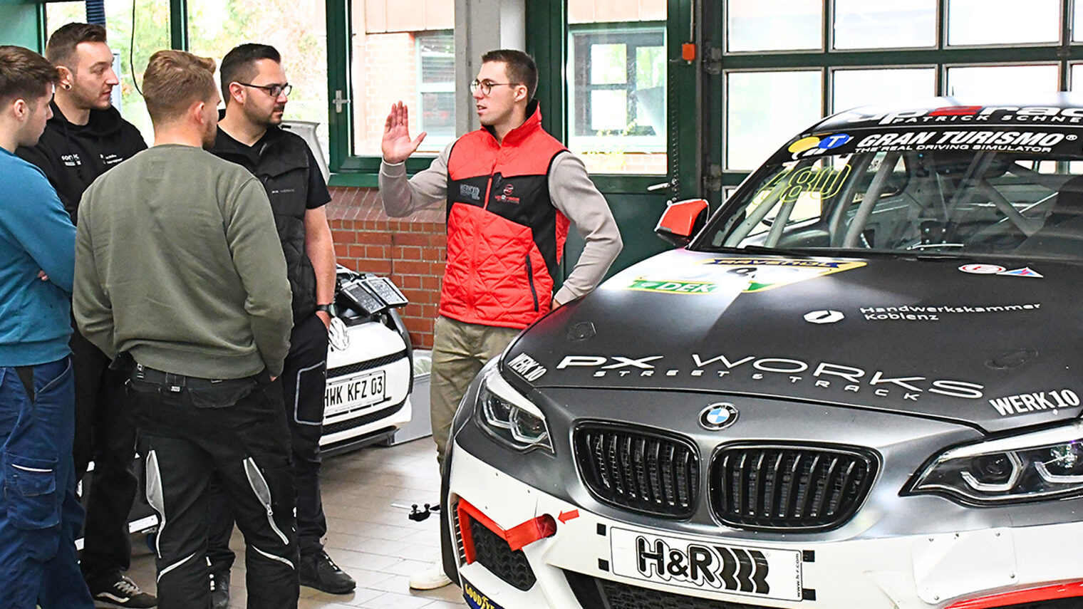 Jannik Reinhard unterhält sich neben einem Auto mit den Meisterschülern.