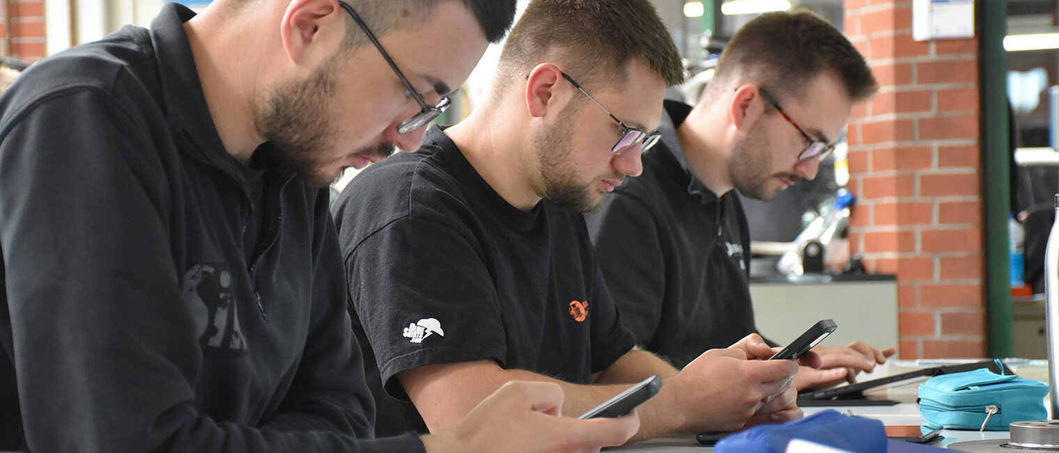 Drei Männer arbeiten im Unterricht mit Handy und Tablet. Drei Männer arbeiten im Unterricht mit Handy und Tablet.