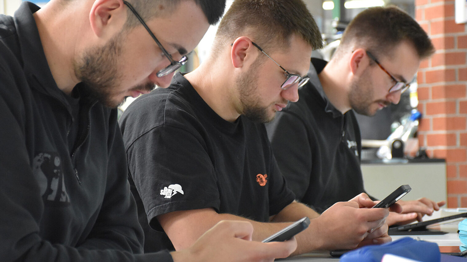 Drei Männer arbeiten im Unterricht mit Handy und Tablet.