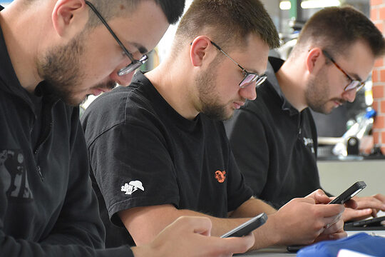 Drei Männer arbeiten im Unterricht mit Handy und Tablet.