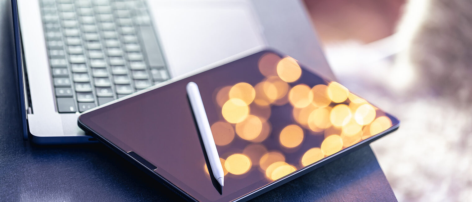 Tablet und Stift auf einem aufgeklappten Laptop