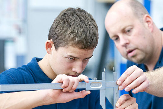 Ausbilder zeigt Lehrling den Umgang mit einer Schieblehre